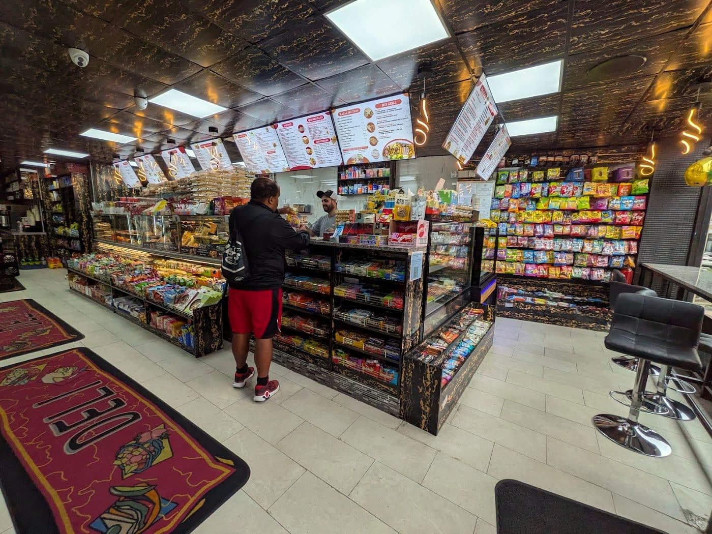 Inside NYC Style Deli, a clean and spacious bodega aisle with the menu boards above the counter